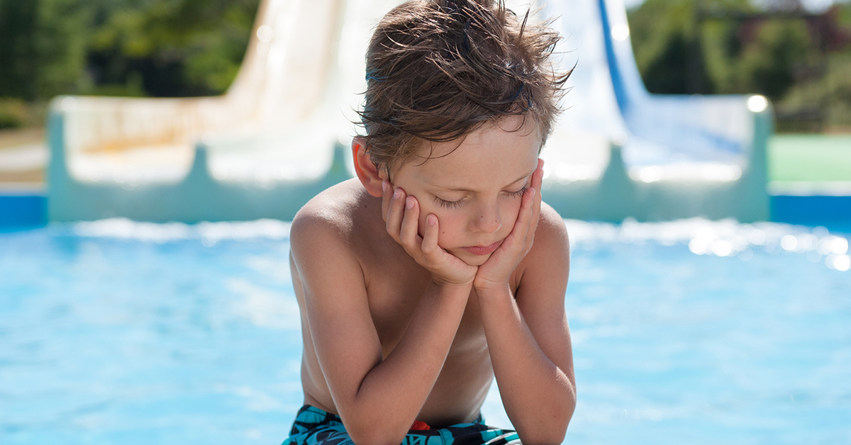 sad little boy sitting near a pooln waiting to swim