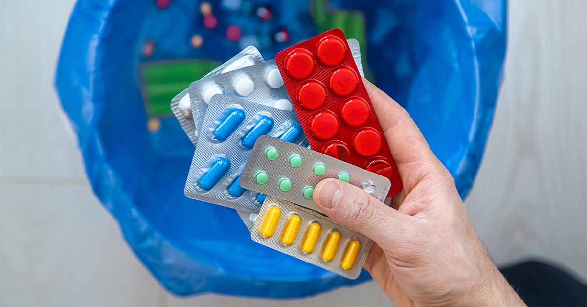 A handful of medications being thrown into a garbage can