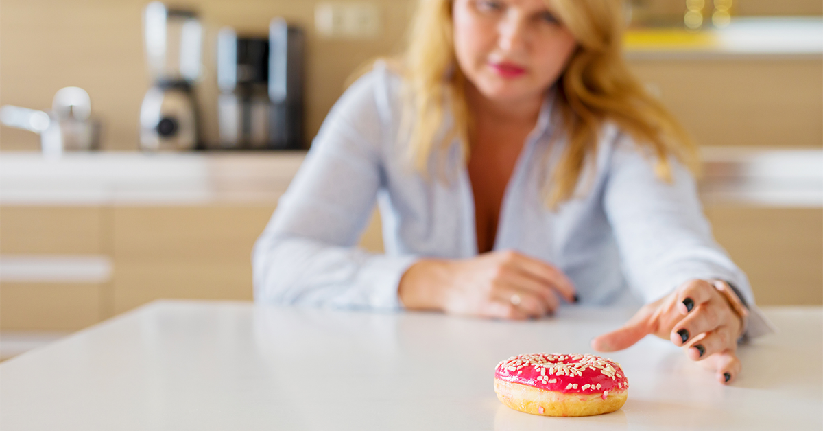 Woman at the kitchen table reaching for a donut.